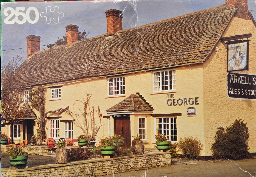 A traditional English stone pub named The George with cream walls, a shingled roof, and an outdoor patio area.