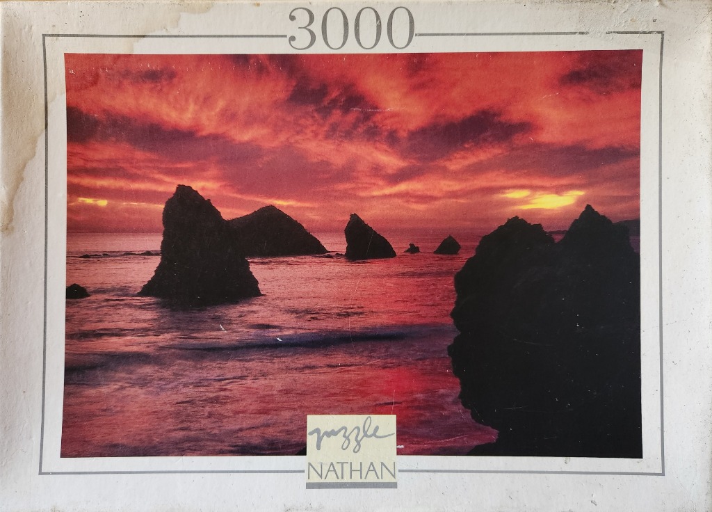 Rocky coastline silhouettes against a vivid crimson sunset over the ocean.