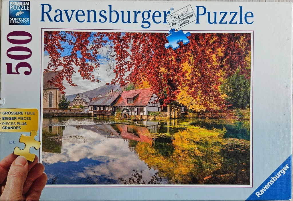A peaceful German timber-framed mill reflected in a calm pond during autumn with vibrant red and gold foliage.