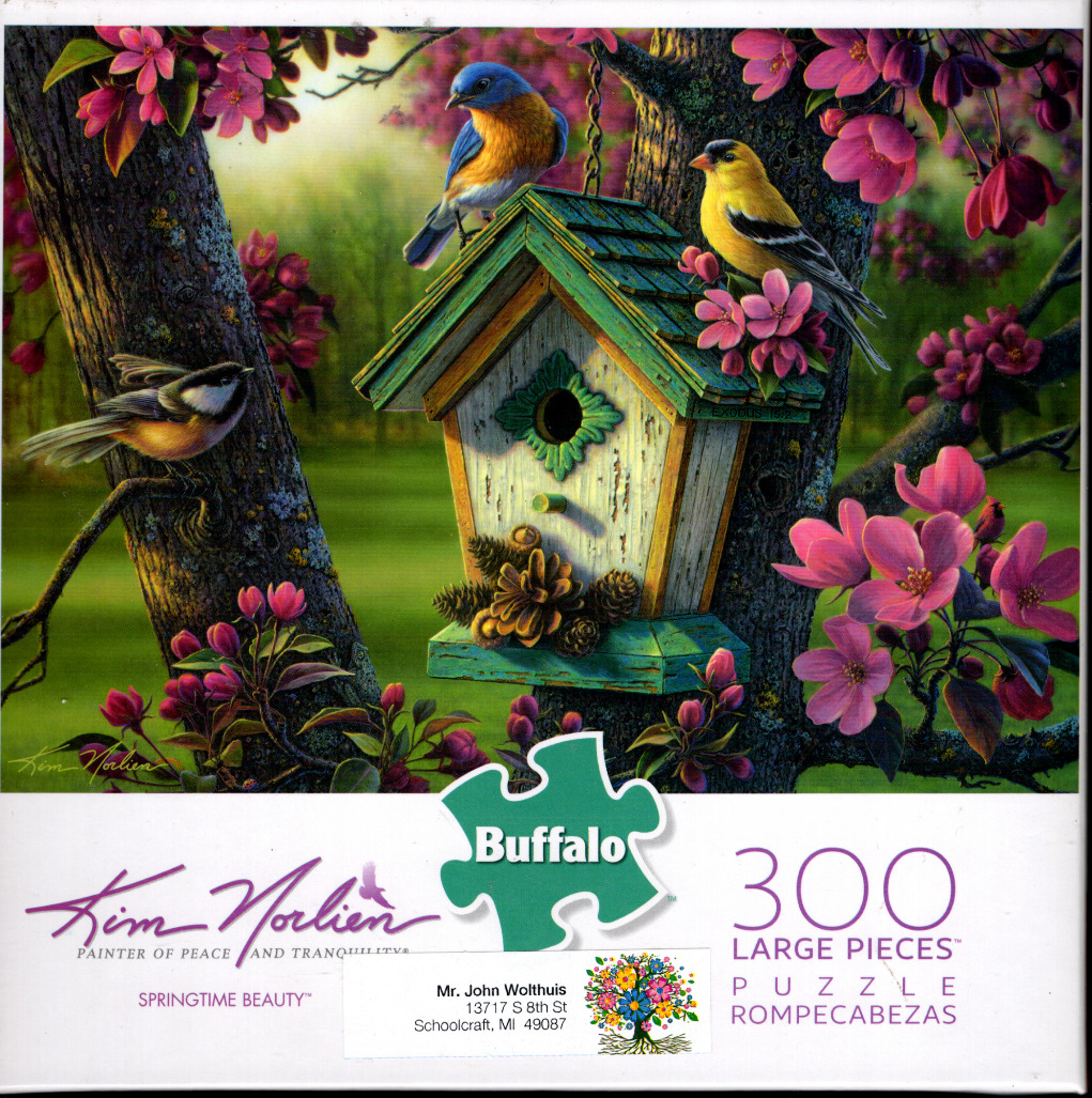 A birdhouse nestled in a tree surrounded by pink blossoms with three small songbirds nearby.