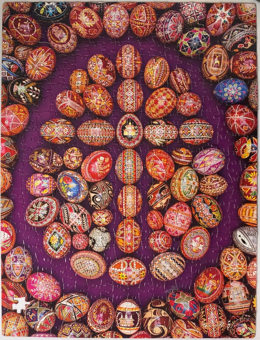A collection of intricately patterned, multi-colored Ukrainian-style Easter eggs arranged against a solid deep purple backgro