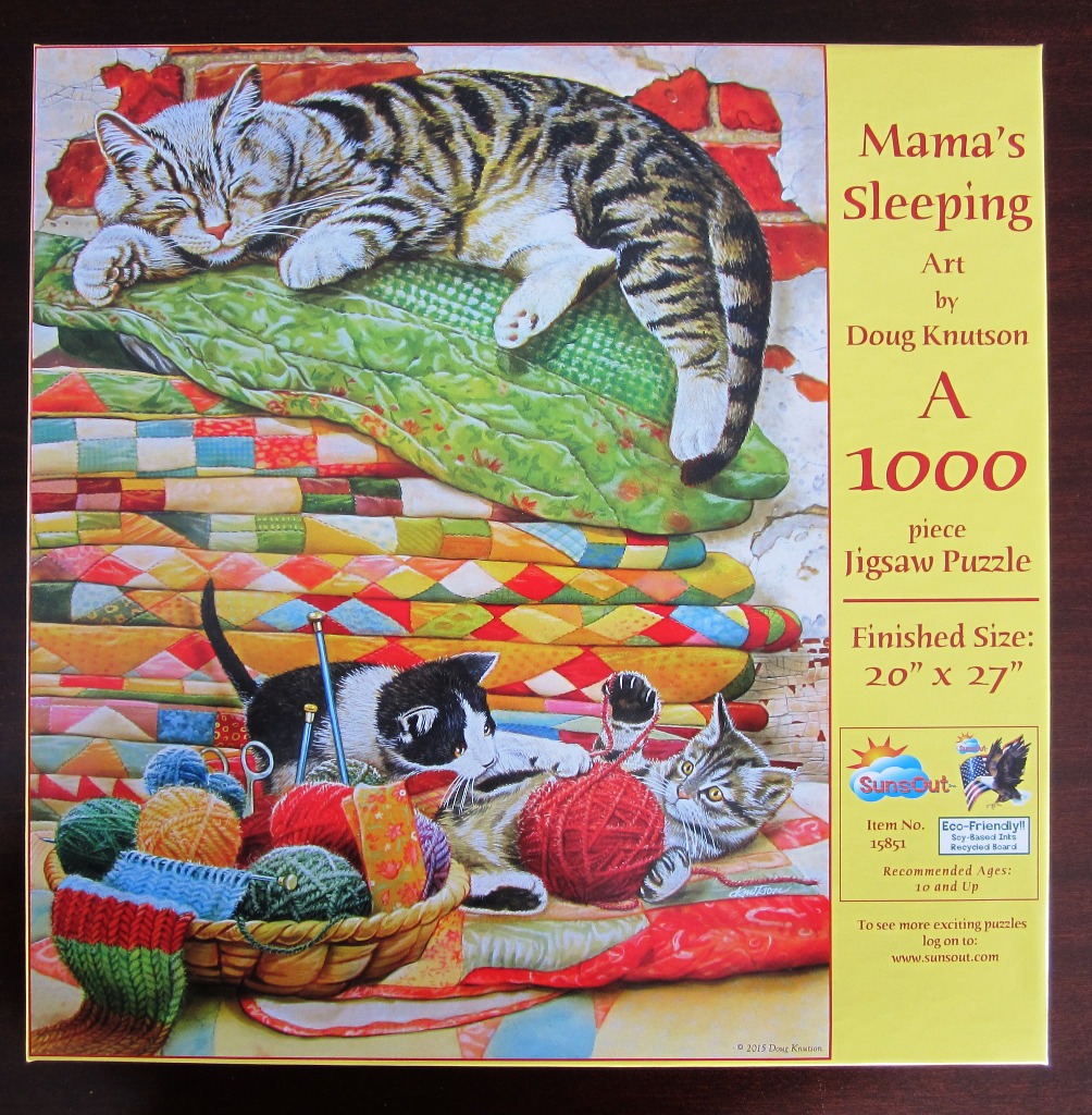 A tabby cat sleeping on stacked quilts with two kittens playing with yarn below.