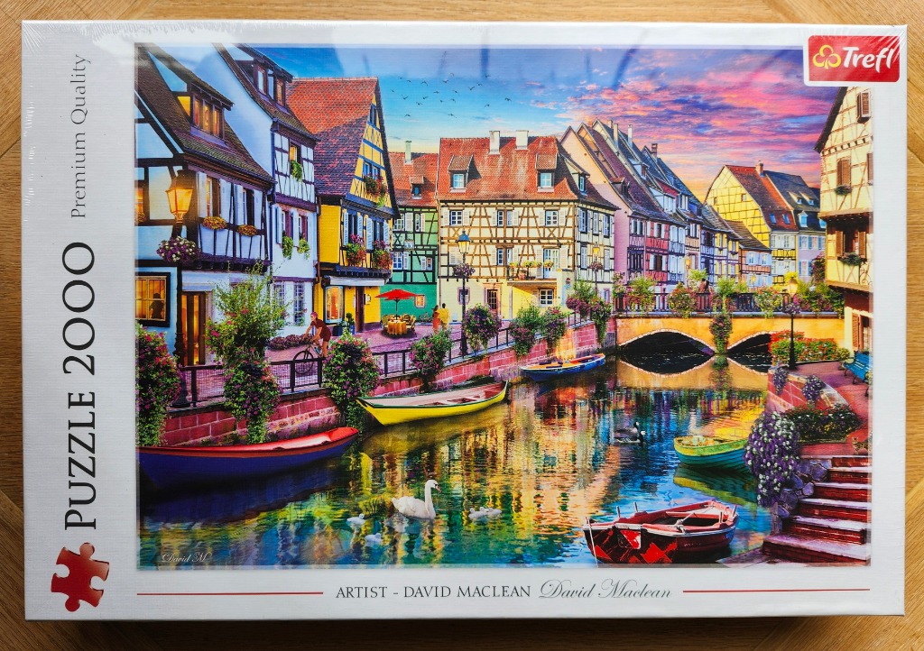 A picturesque European village scene with half-timbered houses, a canal, and a swan at sunset.