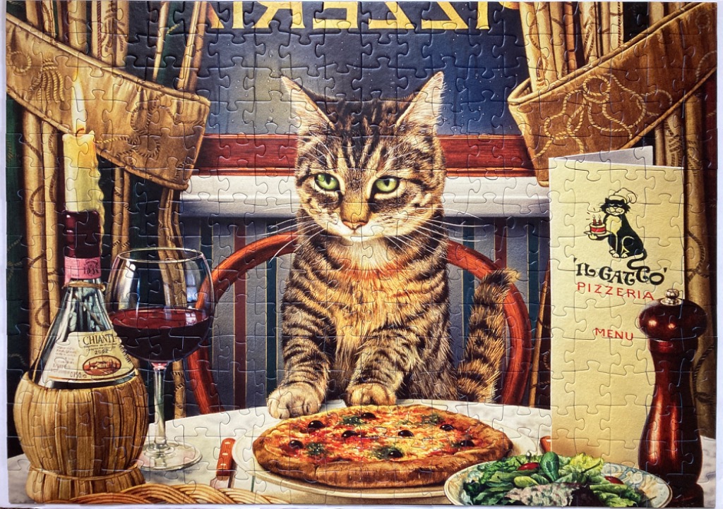 A tabby cat sits at a restaurant table with pizza, wine, and a menu.