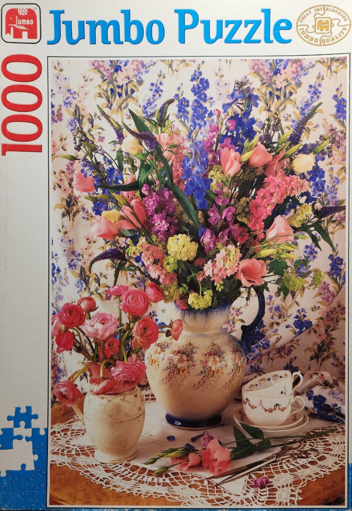 Still life photograph of a floral arrangement in ceramic pitchers and tea cups on a lace tablecloth.