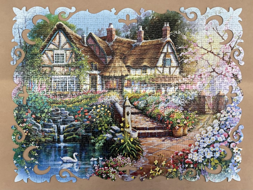 A charming English cottage with a thatched roof, blooming garden, pond with a swan, and a decorative ornate frame border.
