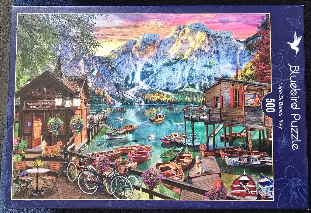 A peaceful lakeside scene at Lago di Braies in Italy with wooden boat houses, colorful boats, and mountain peaks.
