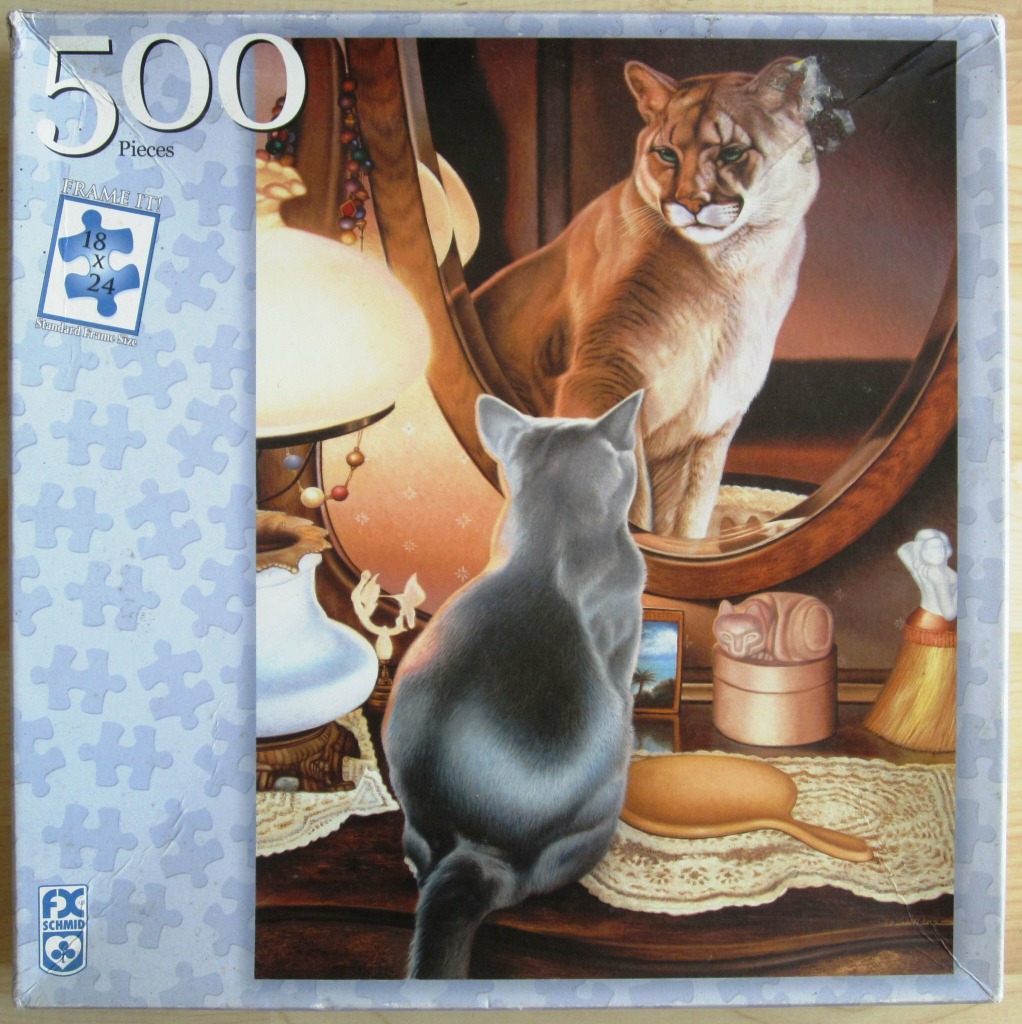 A grey cat sits on a vanity table, looking into a mirror where it sees a mountain lion reflected.
