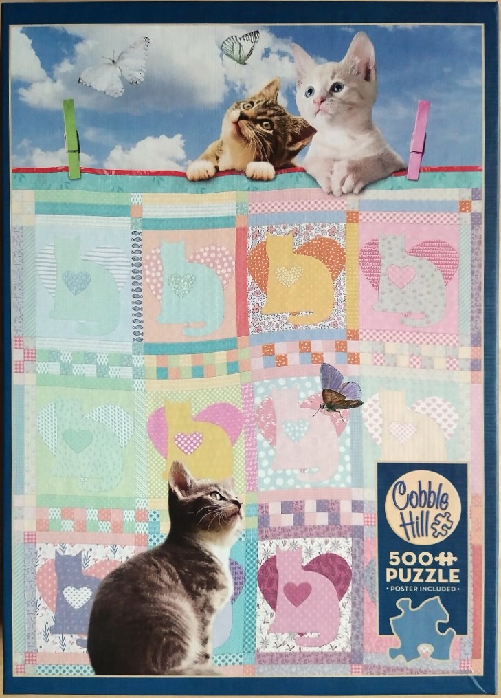 Three kittens sitting on or in front of a patchwork quilt with cat and heart motifs, set against a blue sky.