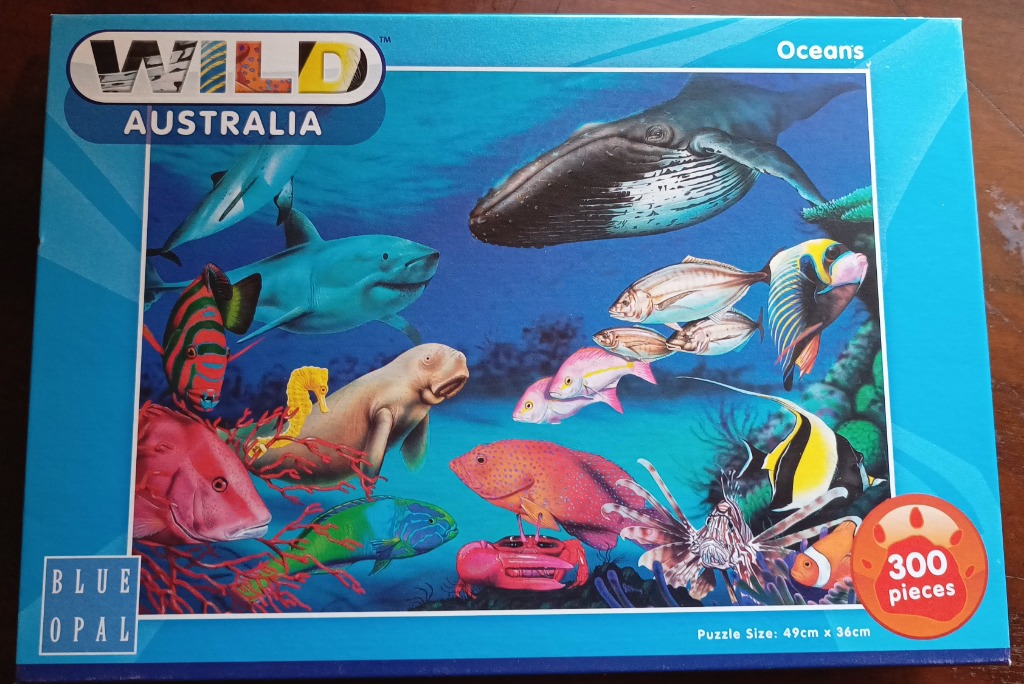 Underwater scene featuring a humpback whale, various sharks, a dugong, and numerous colorful reef fish.