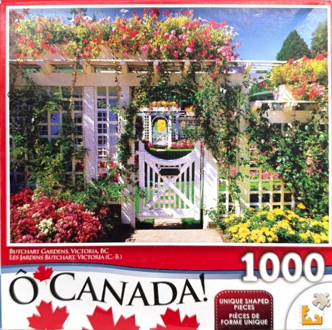 A sunny, white wooden trellis gate surrounded by vibrant red, pink, and yellow flowers at Butchart Gardens.