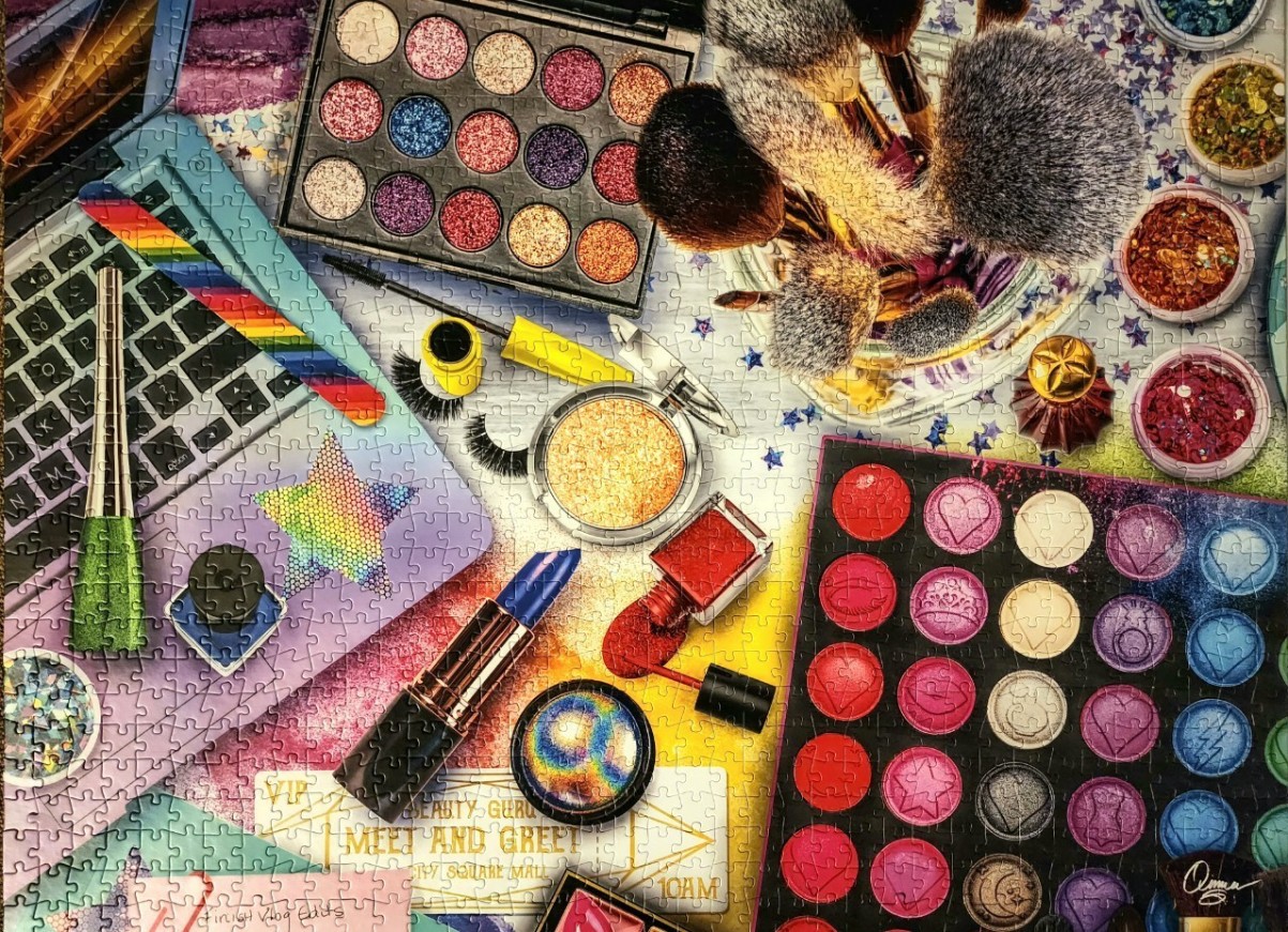 A top-down view of a colorful collection of cosmetics including makeup palettes, brushes, and a laptop.