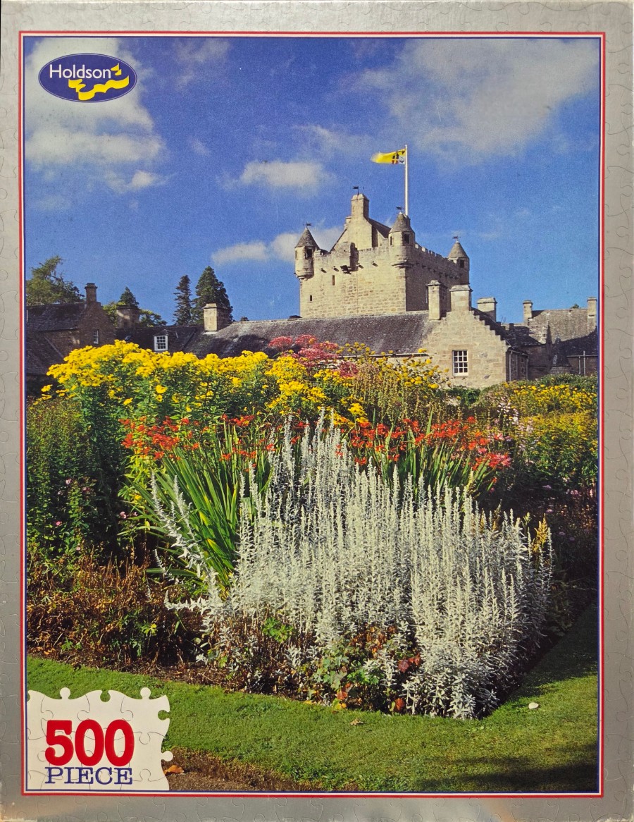 A sunny Scottish castle garden filled with vibrant yellow flowers, silver foliage, and red blooms against a blue sky.