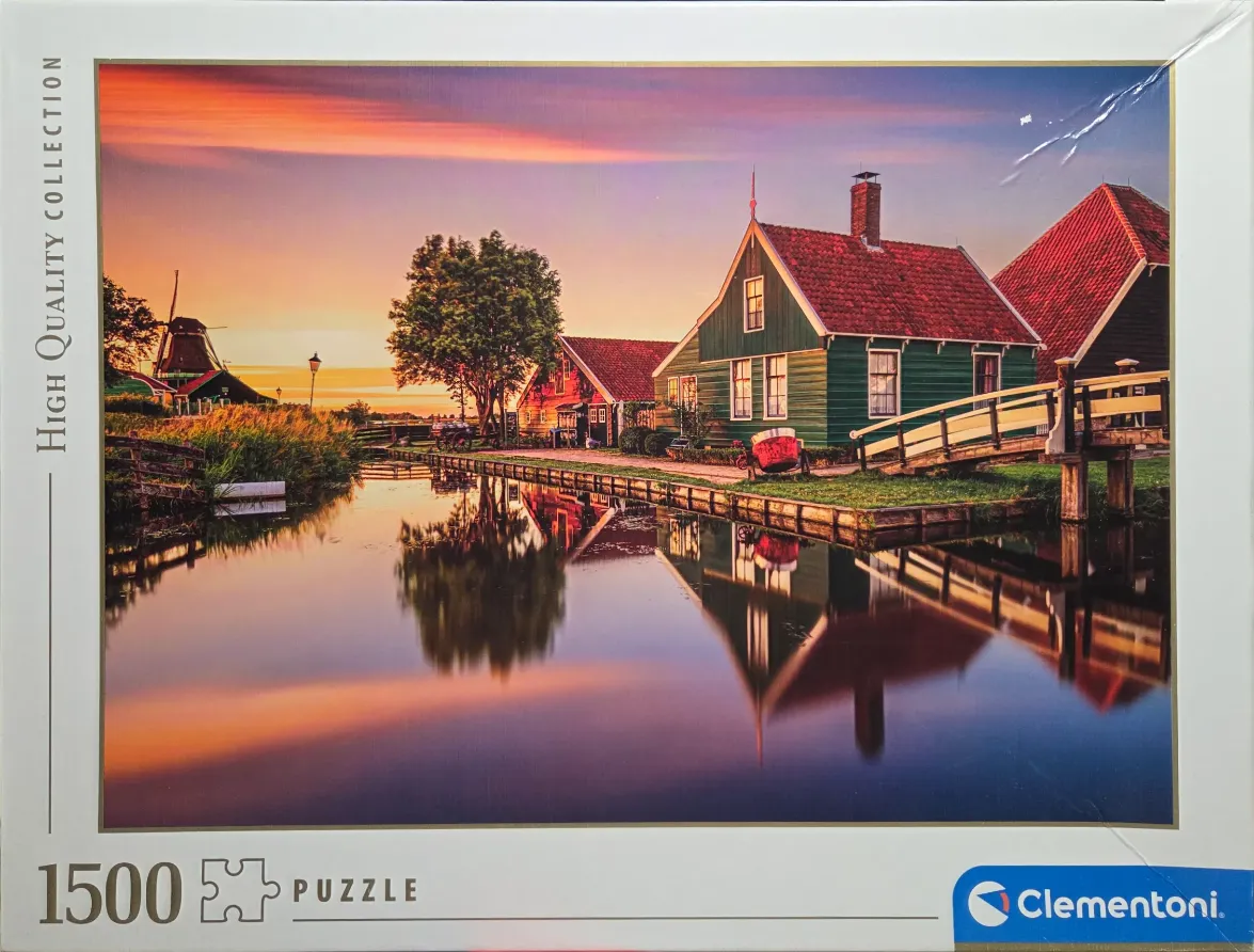 A peaceful Dutch canal scene at sunset with green wooden houses, a traditional windmill, and golden hour reflections.