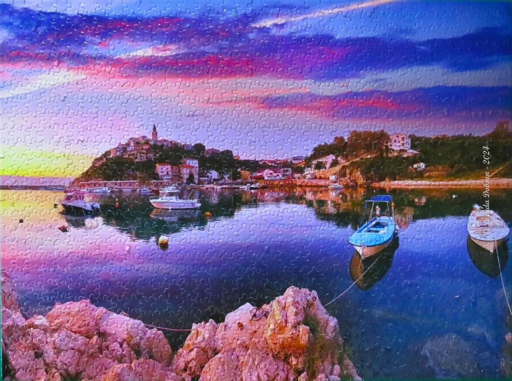 Coastal Mediterranean town at sunset with boats in a calm harbor.