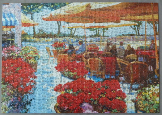 Impressionistic painting of an outdoor cafe terrace filled with red flowers under umbrellas.