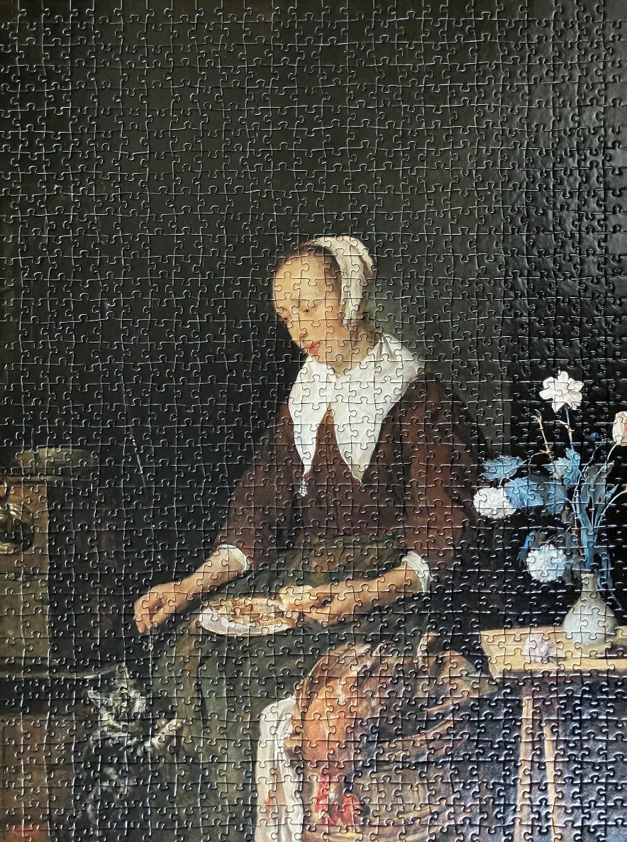 A woman in a white cap and brown dress sitting at a table with a bouquet of flowers and a cat.