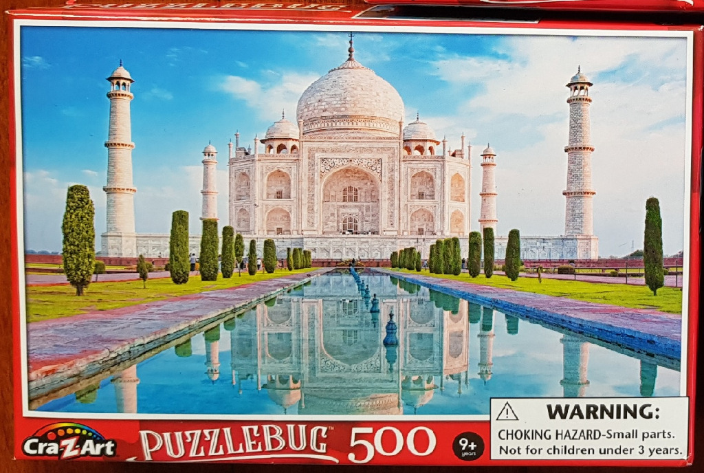 The Taj Mahal viewed from the front, reflected in a long rectangular water feature amidst landscaped gardens.
