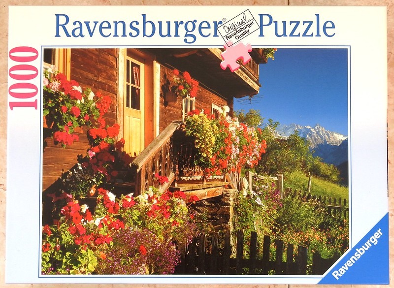 A traditional wooden Alpine chalet decorated with vibrant red flowers and a backdrop of snow-capped mountains.
