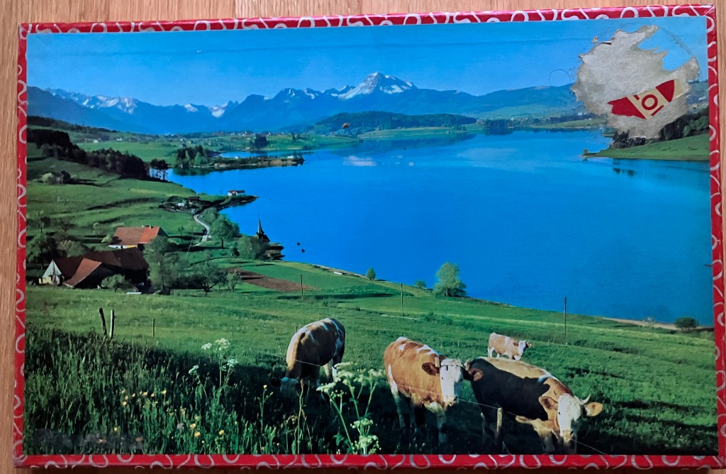 Scenic landscape of a blue lake in the Swiss Alps with grazing cows in the foreground.