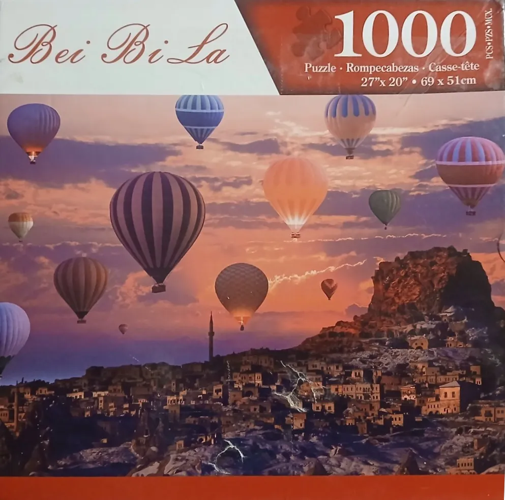 A panoramic view of hot air balloons floating over a town in Cappadocia at sunset.