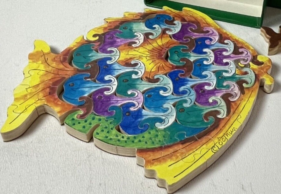 A fish-shaped object decorated with an Escher-style tessellation of interlocking fish in vibrant watercolor tones.