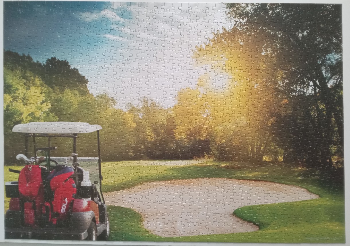 A golf cart parked near a sand bunker on a sunlit golf course surrounded by trees.