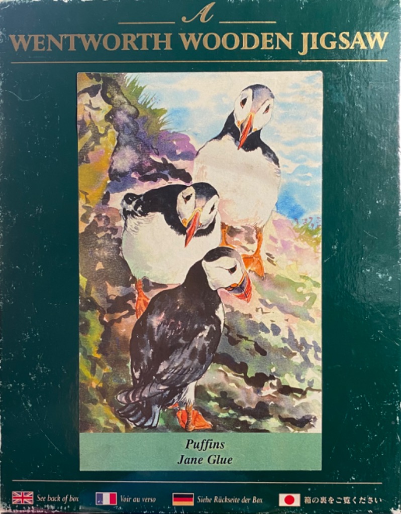 A watercolor painting of three puffins standing on a rocky coastal cliff.