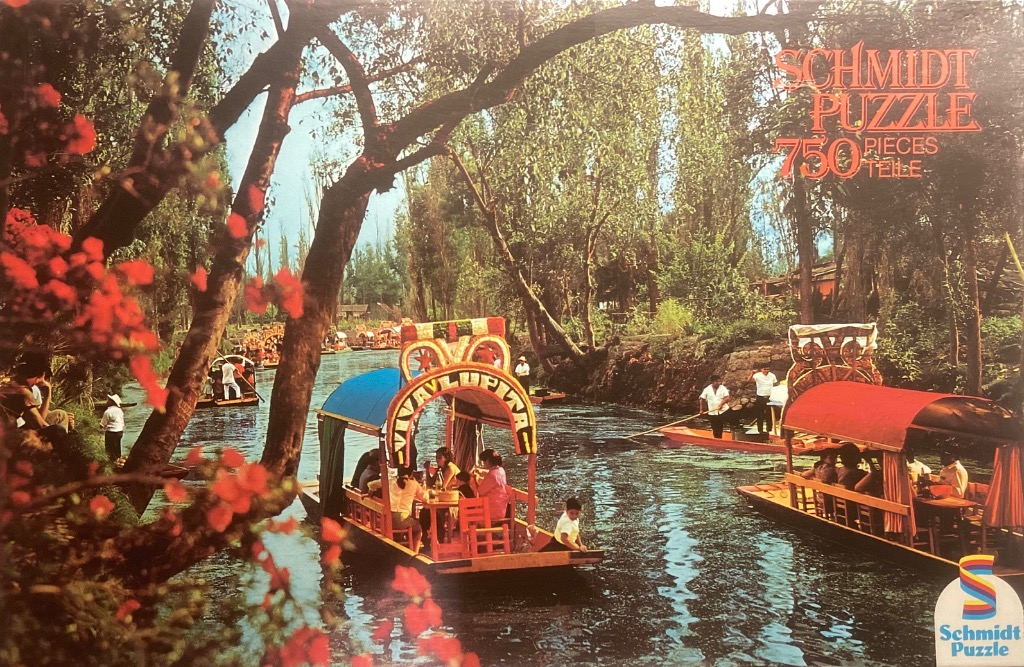 Colorful tourist boats traversing a sunlit canal in Xochimilco, Mexico, surrounded by lush trees and red flowers.