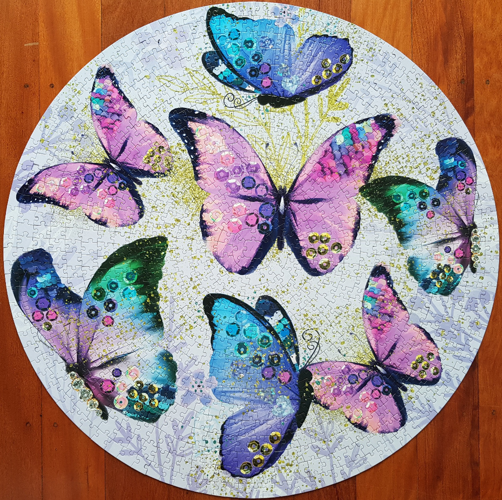Circular illustration of six colorful butterflies decorated with shimmering sequins on a light background.