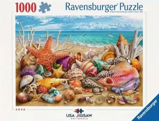 An assortment of seashells, starfish, and coral on a sandy beach by a blue ocean.