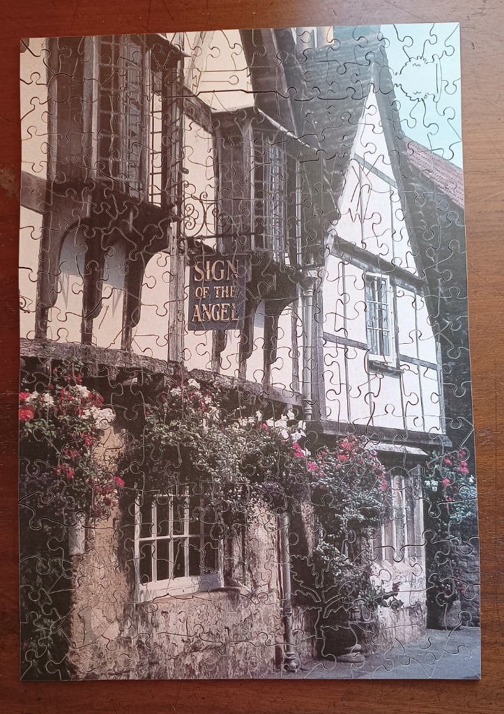 A black and white photograph of an old English building with a hanging sign that reads Sign of the Angel.