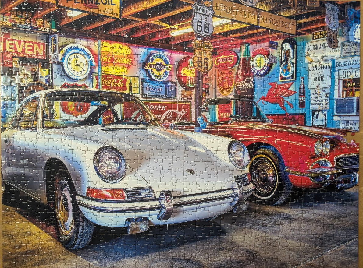 A silver vintage Porsche and a red convertible car parked in a garage filled with Americana advertising signs.