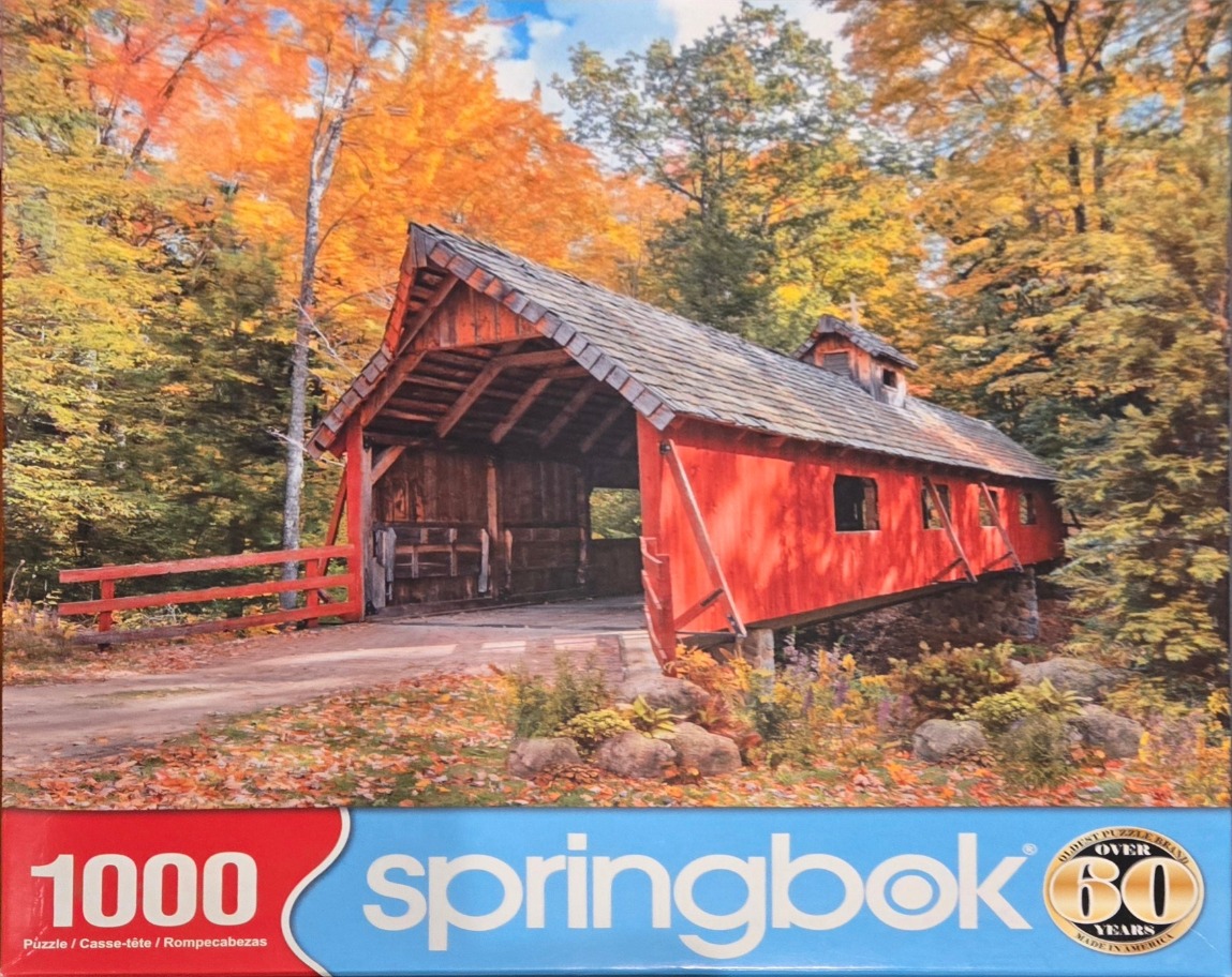 A bright red covered bridge nestled in an autumnal forest with vibrant orange and gold fall foliage.