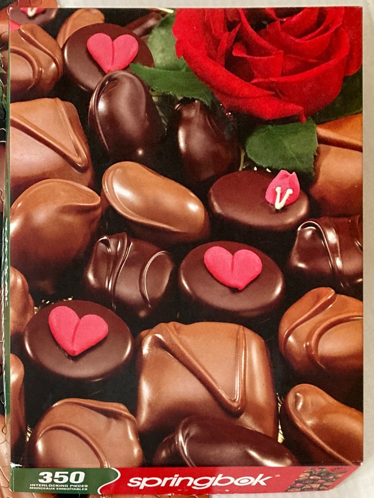 A close-up photograph of assorted chocolates and a vibrant red rose.