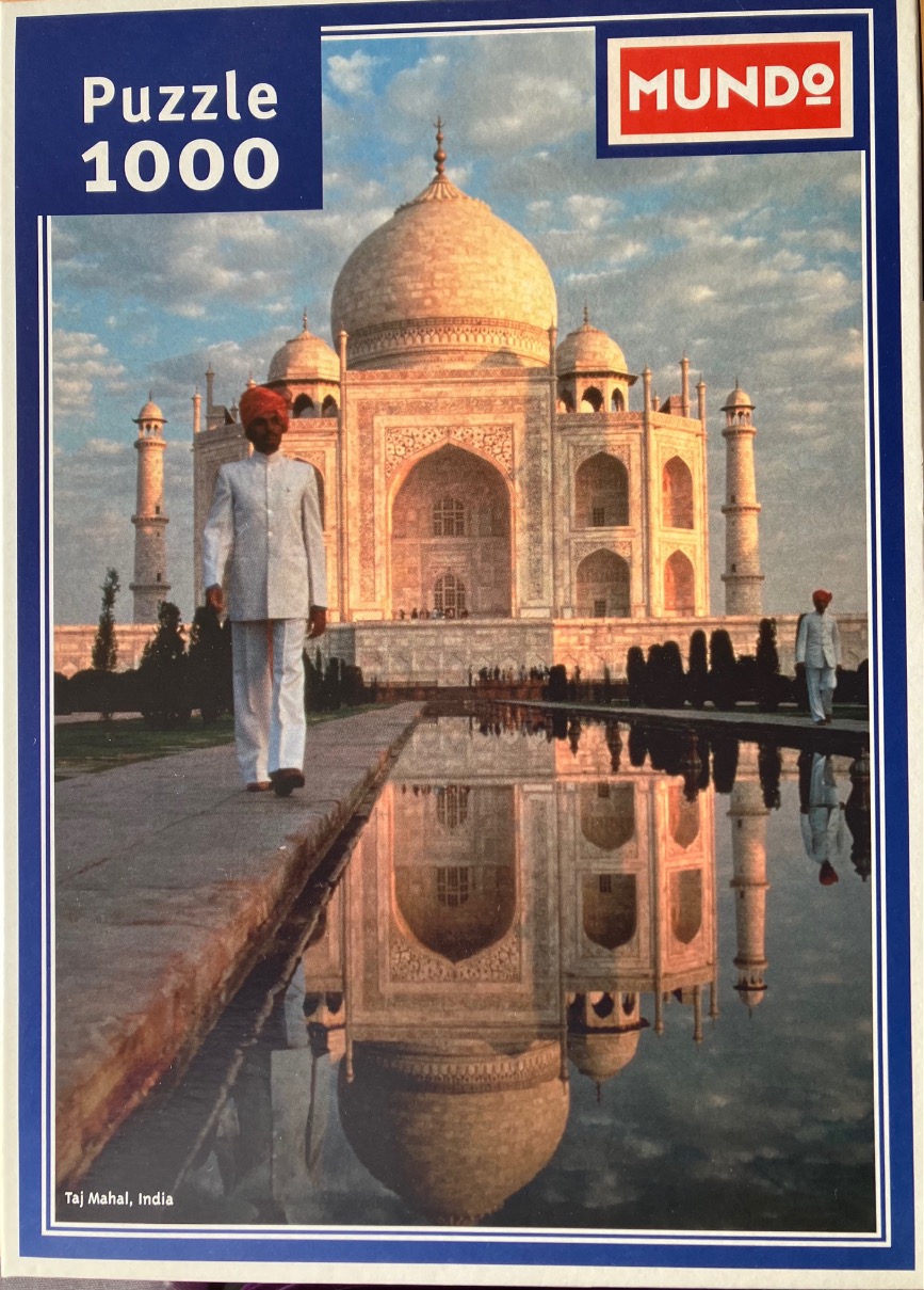 A man in traditional Indian attire walks along a reflecting pool in front of the Taj Mahal at sunset.