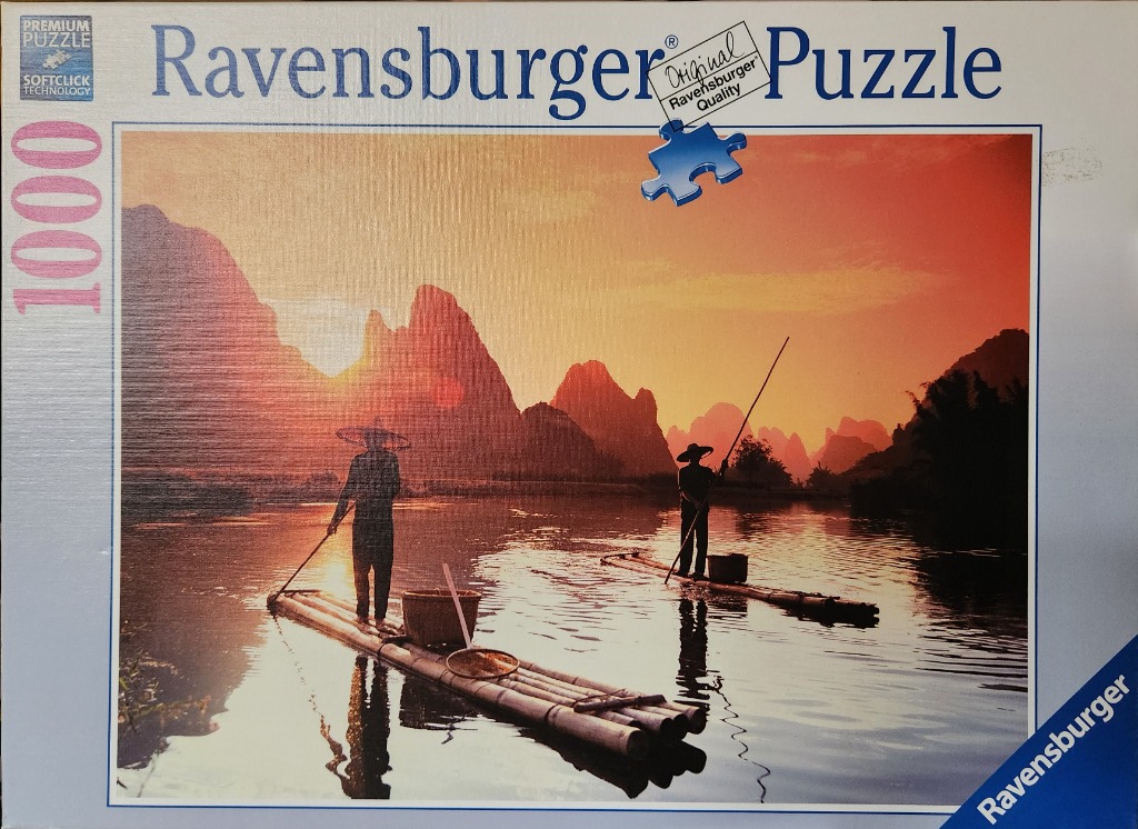 Two fishermen on bamboo rafts on a river at sunset with limestone karst mountains in the background.
