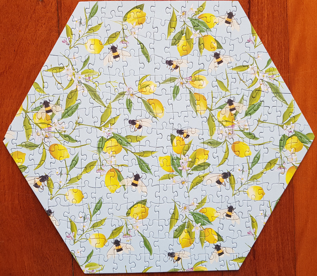 A hexagonal illustration of lemons, green leaves, white blossoms, and honeybees on a light blue background.