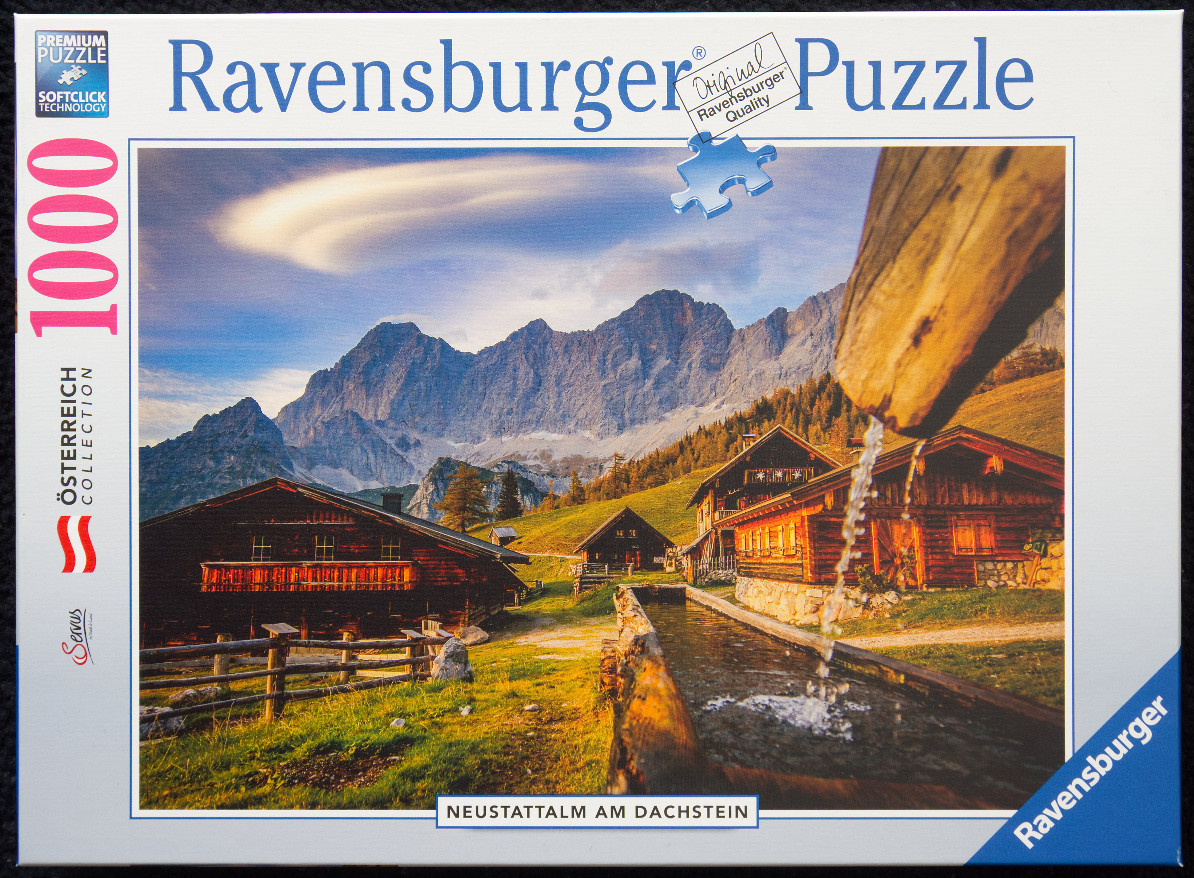 A photograph of traditional wooden alpine huts in the Austrian mountains under a dramatic sky.