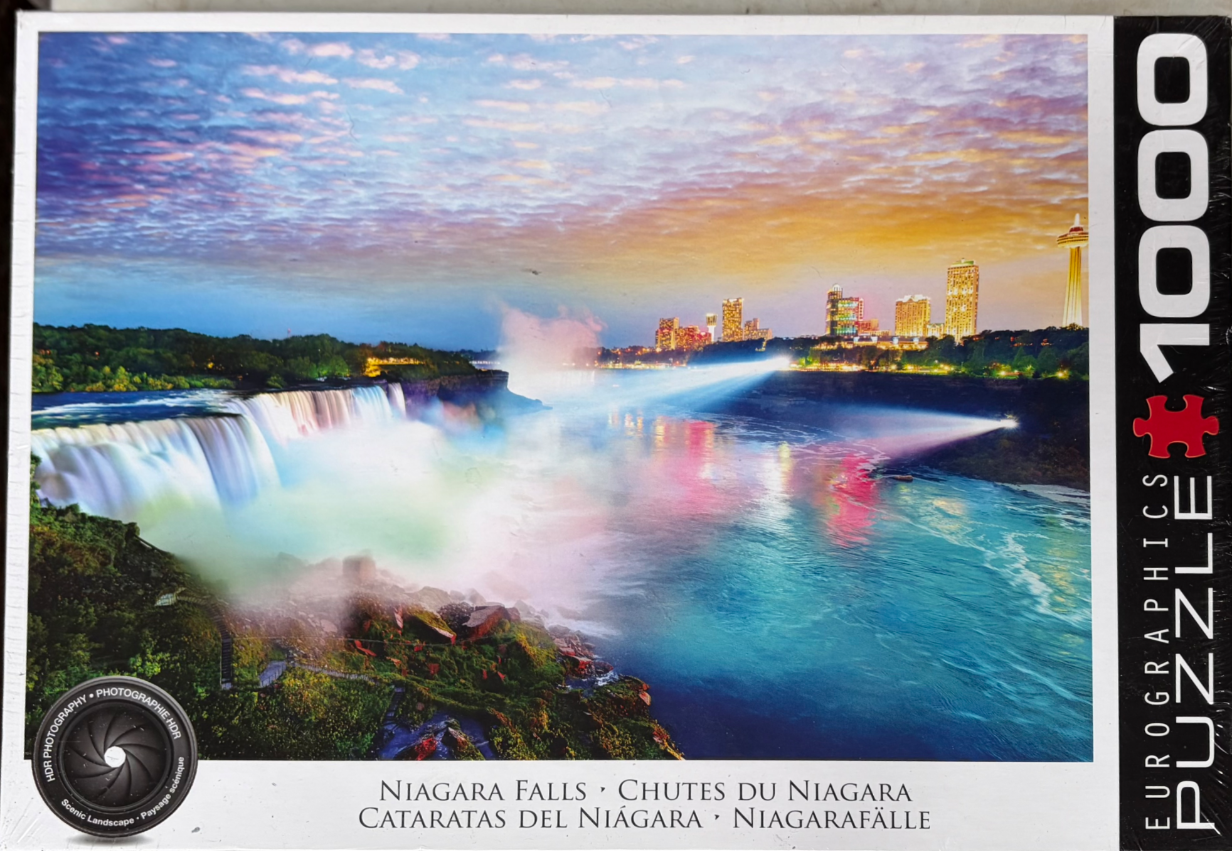 A panoramic long-exposure photograph of Niagara Falls at dusk with the city skyline illuminated in the background.