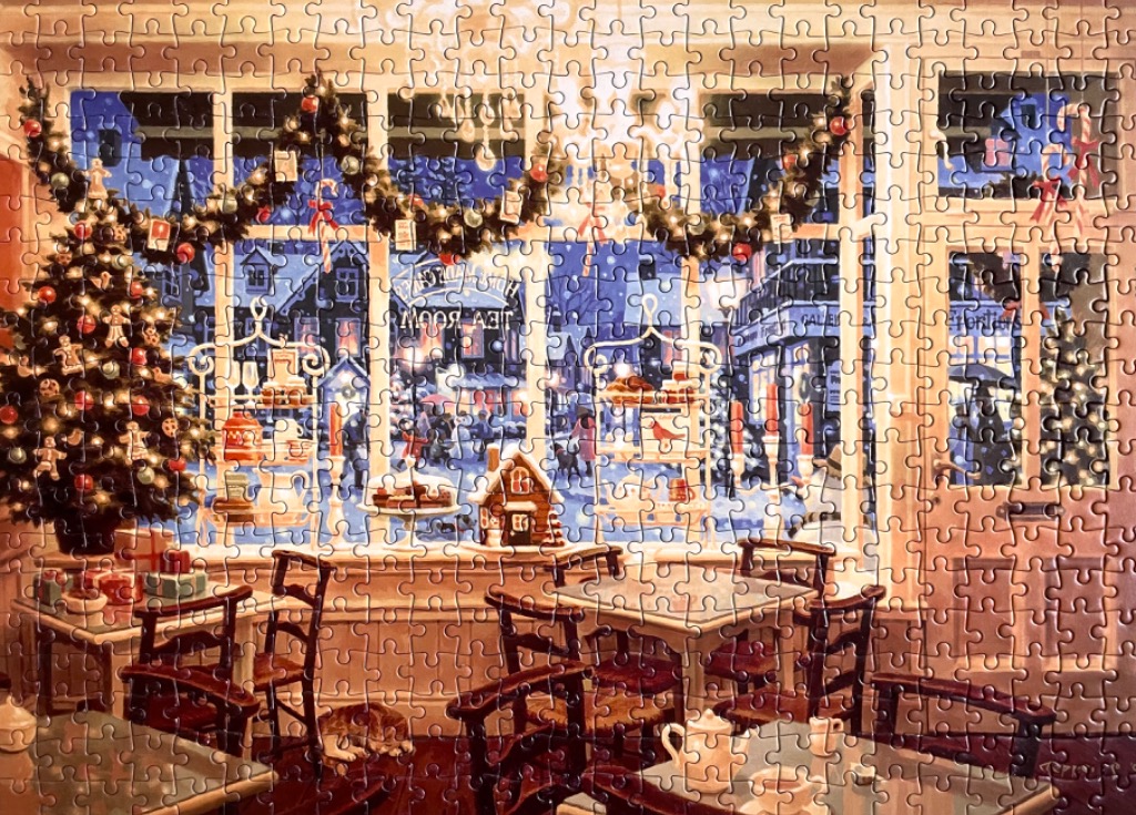 A cozy, snow-covered tea room window at Christmas with a decorated tree and tables.