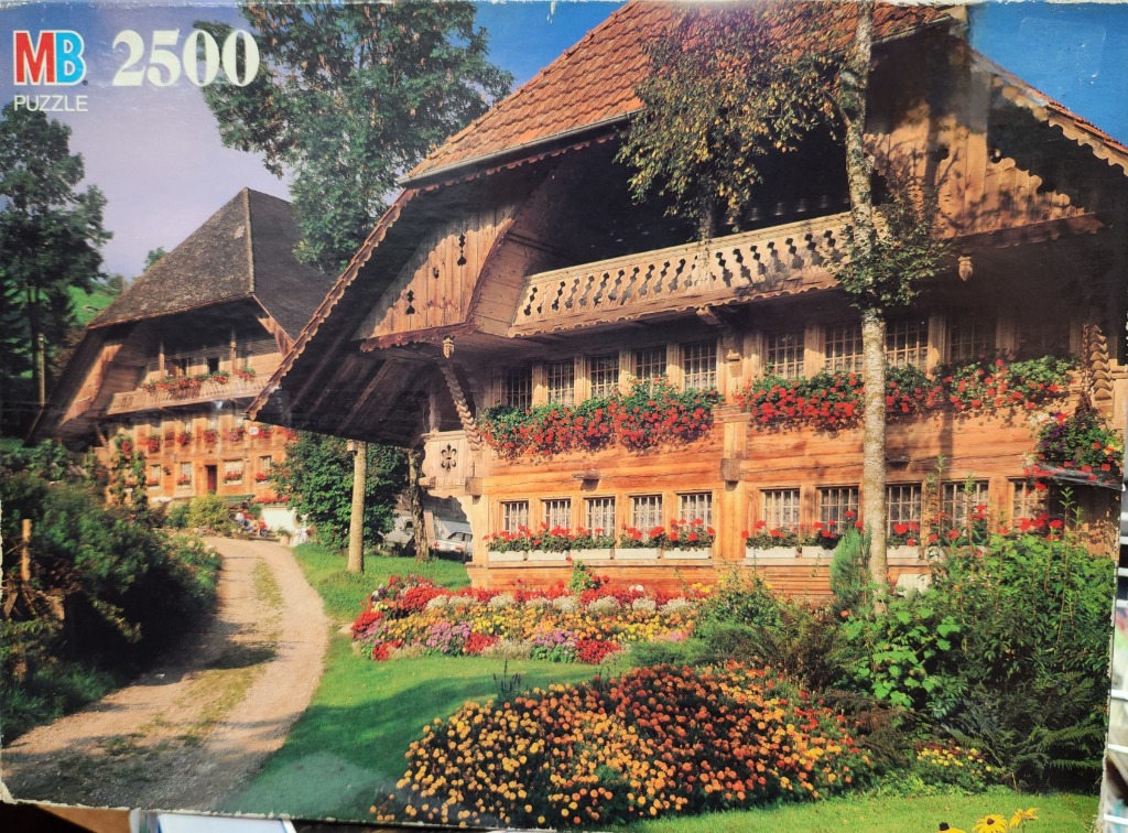 Two traditional Swiss wooden farmhouses with flower-covered balconies set in a lush garden.