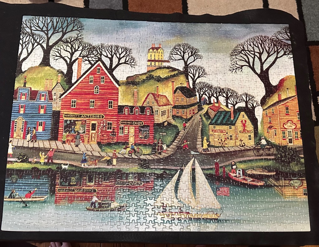 Folk art scene of a coastal town featuring a red antique shop, a yellow cafe, and a sailboat on the water.