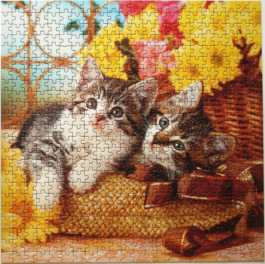Two fluffy tabby kittens peeking out of a woven basket surrounded by yellow sunflowers.