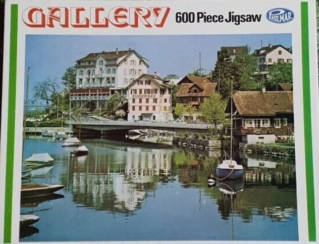 A peaceful lakeside view of a Swiss town with reflections on the water and small boats docked near a bridge.