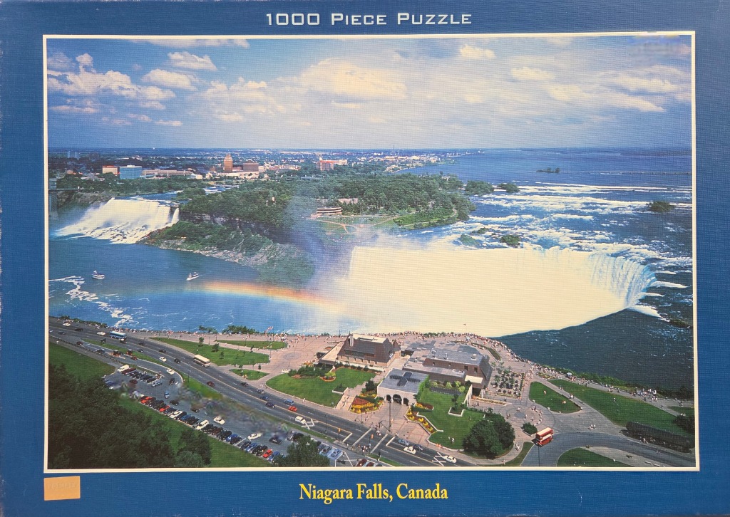 Aerial view of Niagara Falls with a bright rainbow arching over the Horseshoe Falls and the Canadian parkland below.