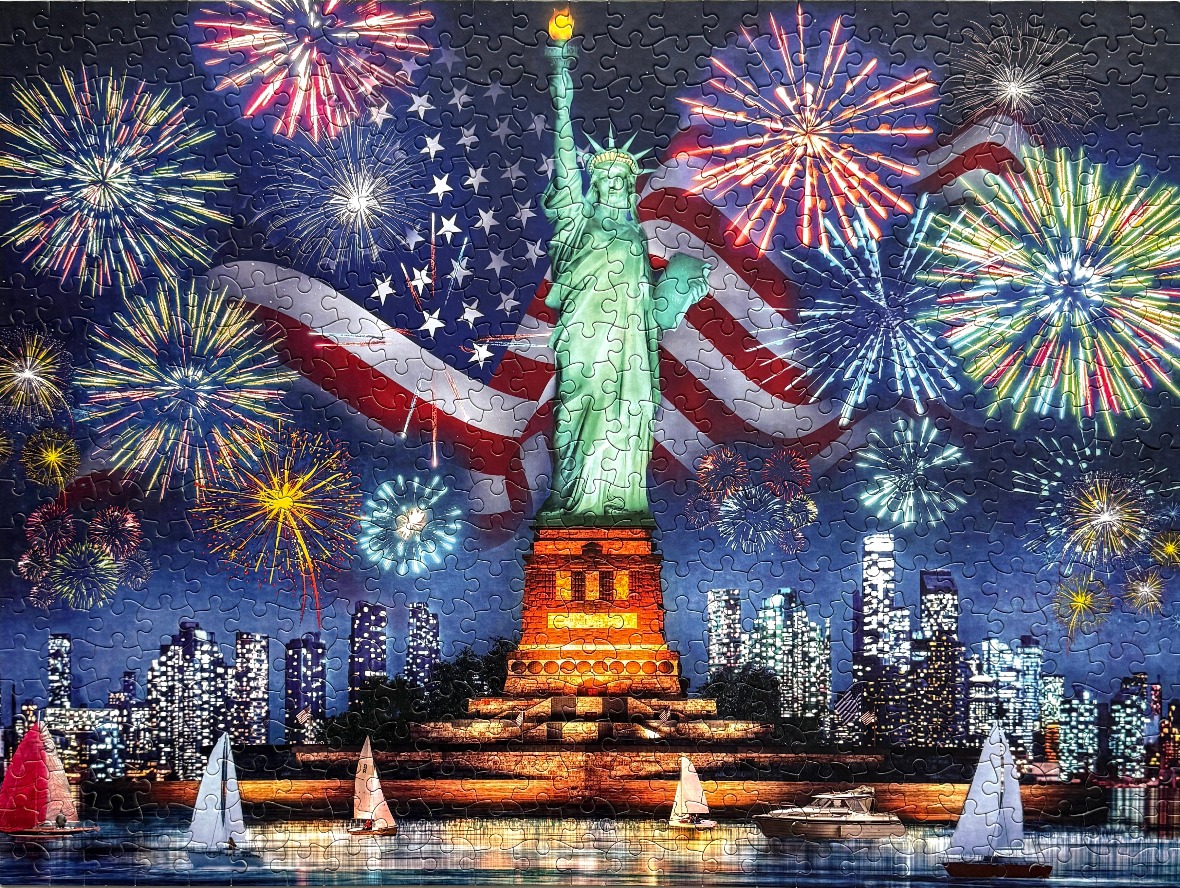 Statue of Liberty illuminated at night against a backdrop of the American flag and colorful fireworks over a city skyline.
