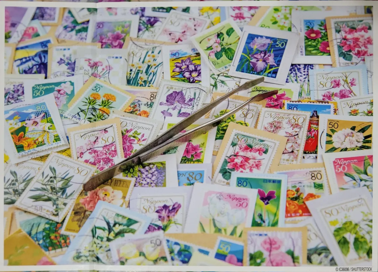 A close-up collage of numerous colorful postage stamps featuring floral designs with a pair of metal tweezers resting atop.