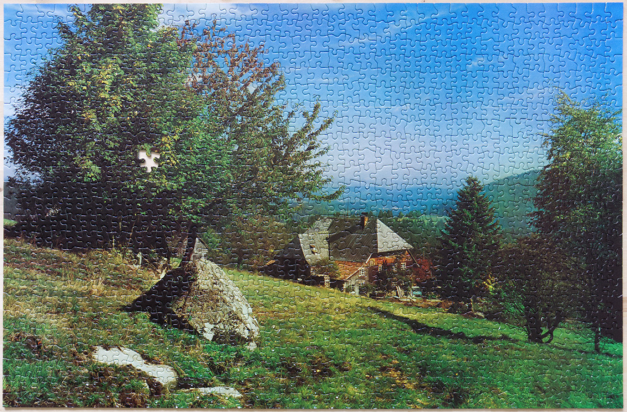 A rustic house nestled in a lush, green mountain landscape under a bright blue sky.