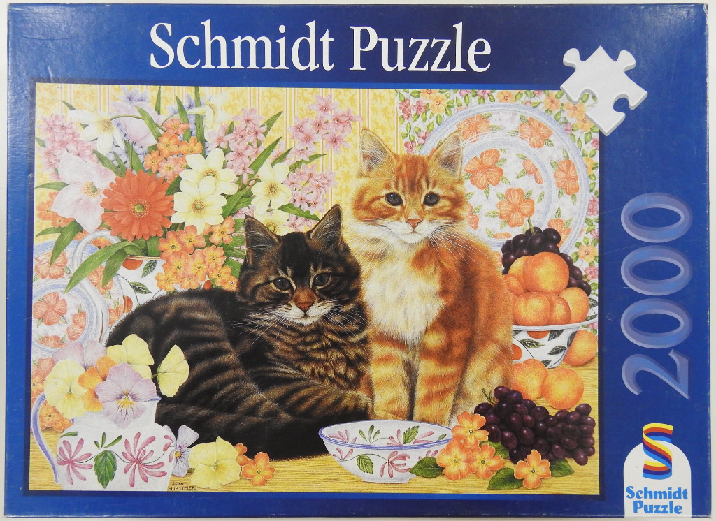 Two cats, one black tabby and one orange tabby, sitting among flowers, fruit, and decorative china.